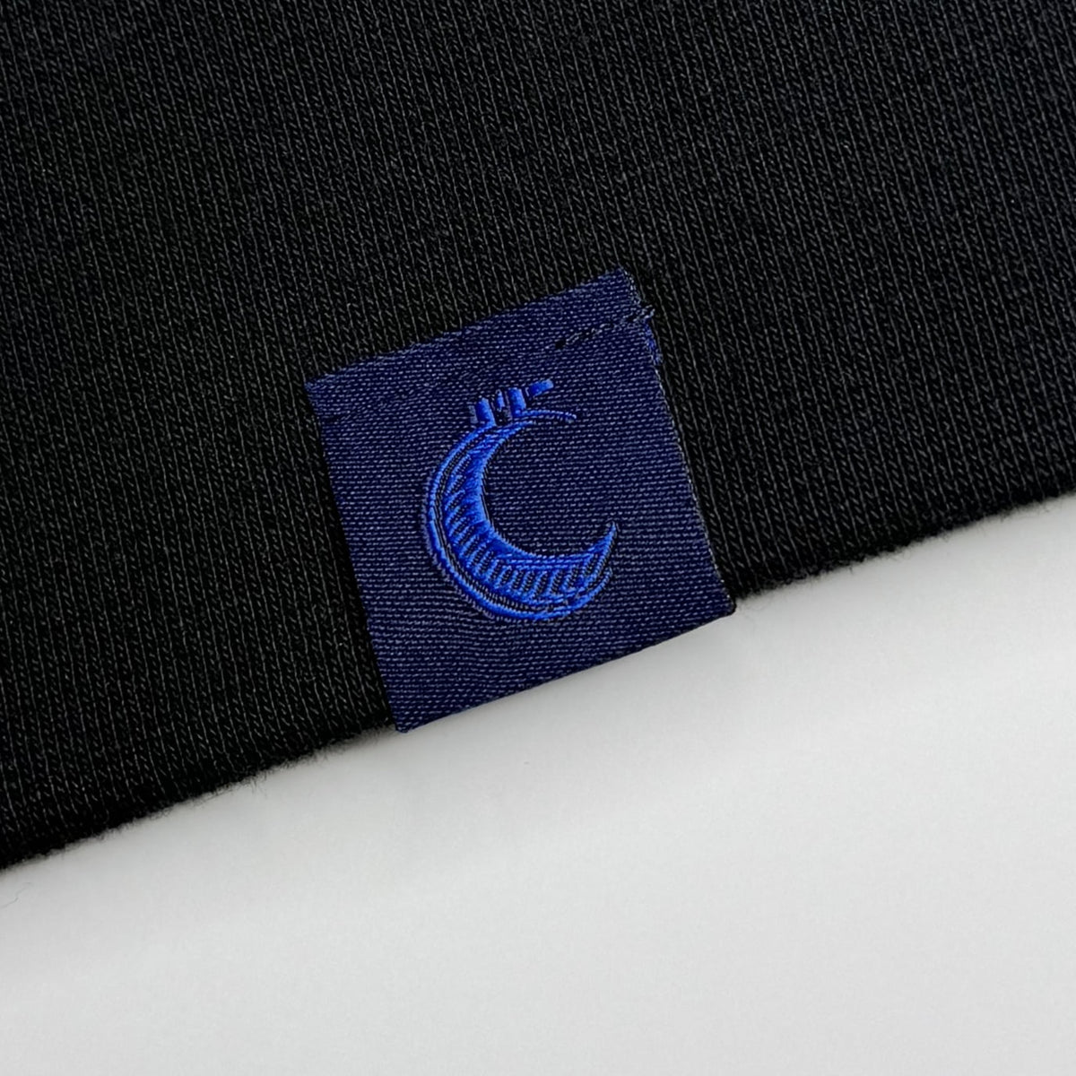 Close-up of the woven brand tag with its crescent moon logo, stitched at the garment hem