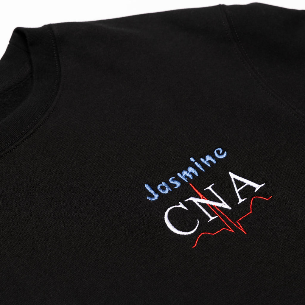Close-up of a custom name and the CNA design embroidered on the chest of the Black crewneck