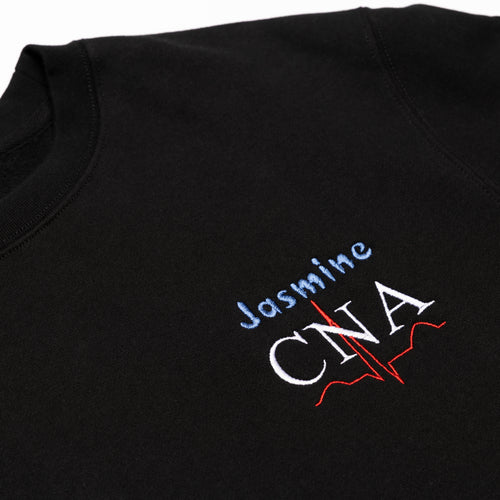Close-up of a custom name and the CNA design embroidered on the chest of the Black crewneck