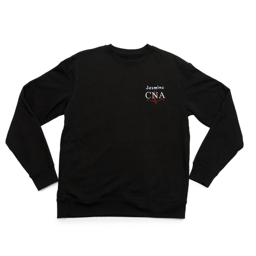 Black crewneck laid flat with a custom name and the CNA design embroidered on the chest