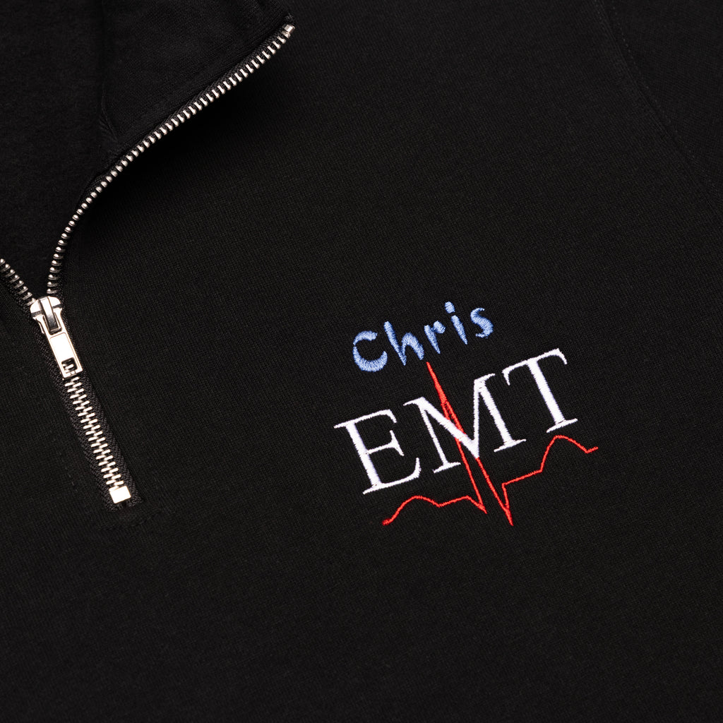 Close-up of a custom name and the EMT design embroidered on the chest of the Black quarter-zip