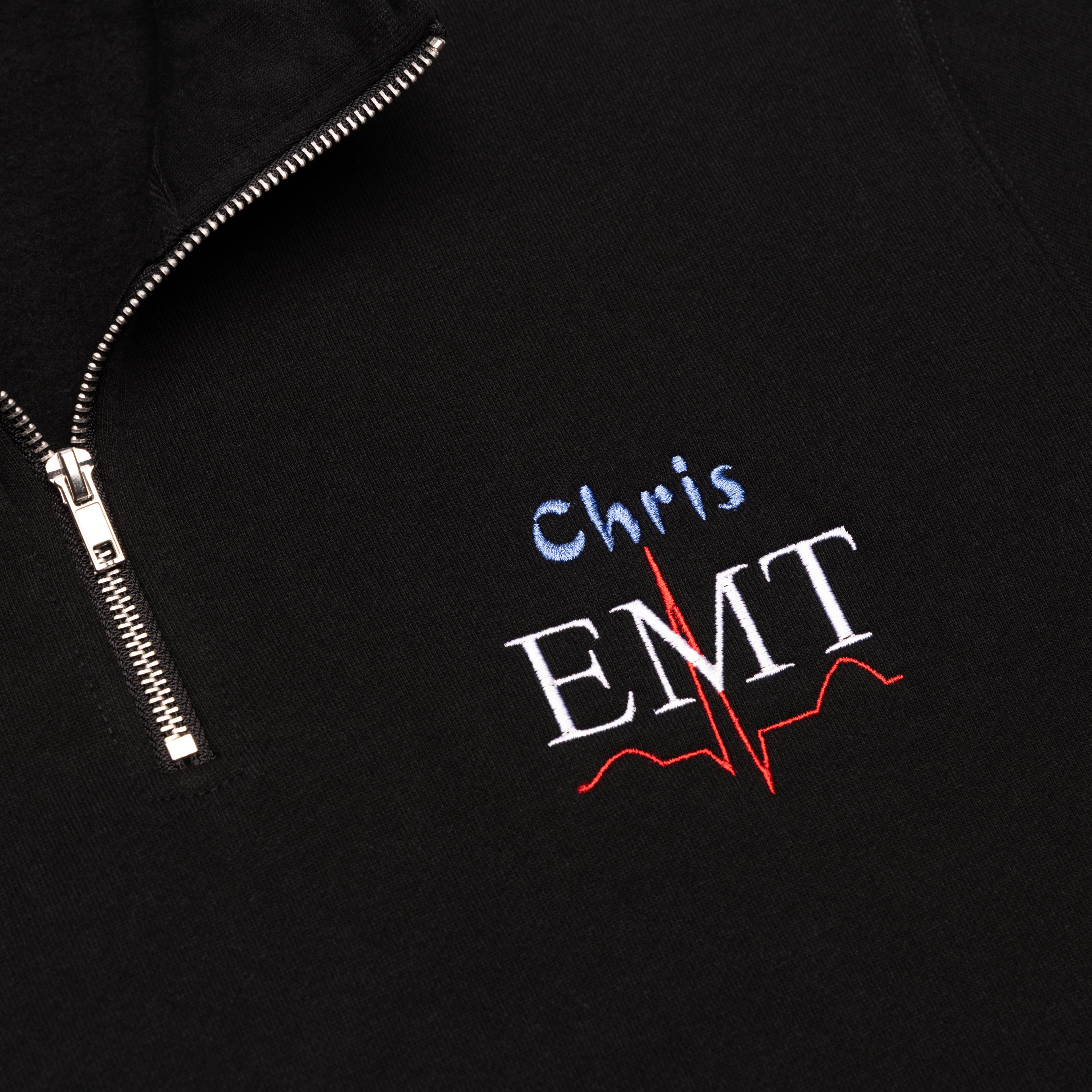 Close-up of a custom name and the EMT design embroidered on the chest of the Black quarter-zip