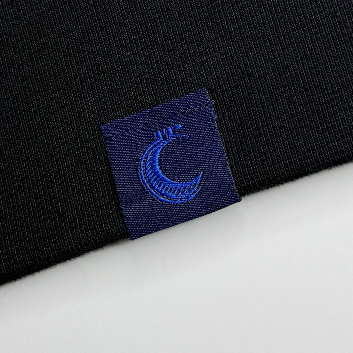 Close-up of the woven brand tag with its crescent moon logo, stitched at the garment hem