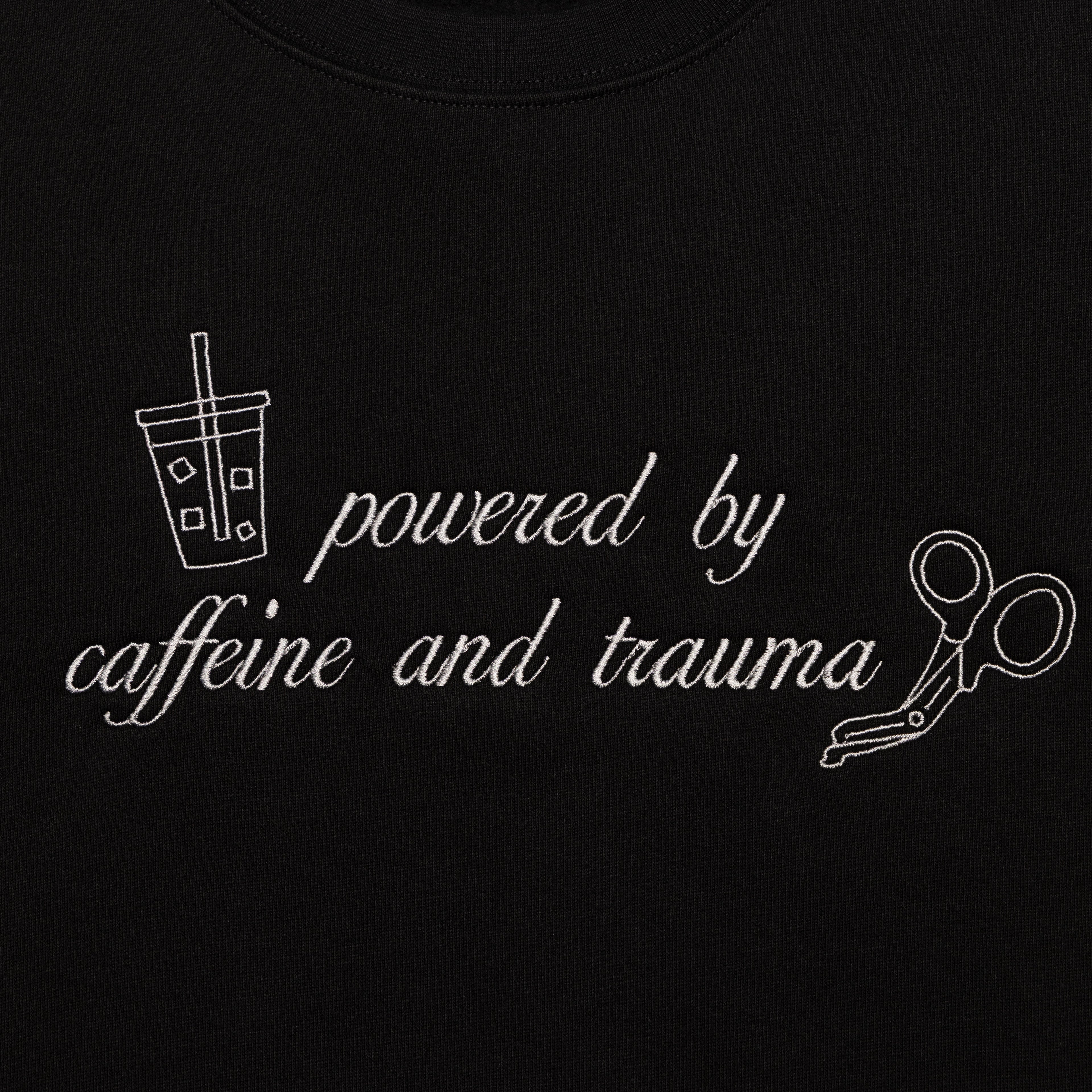 Close-up of the Powered by Caffeine and Trauma design embroidered on the chest of the Black crewneck