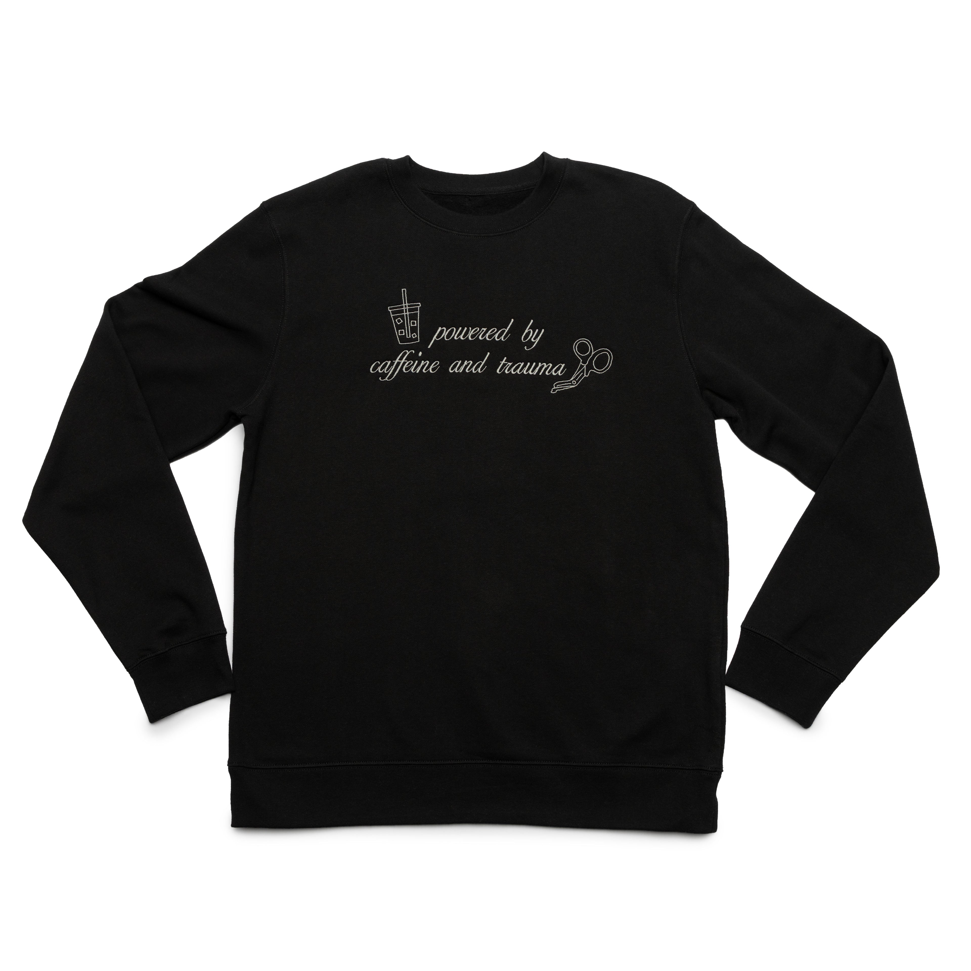 Black crewneck laid flat with the Powered by Caffeine and Trauma design embroidered on the chest