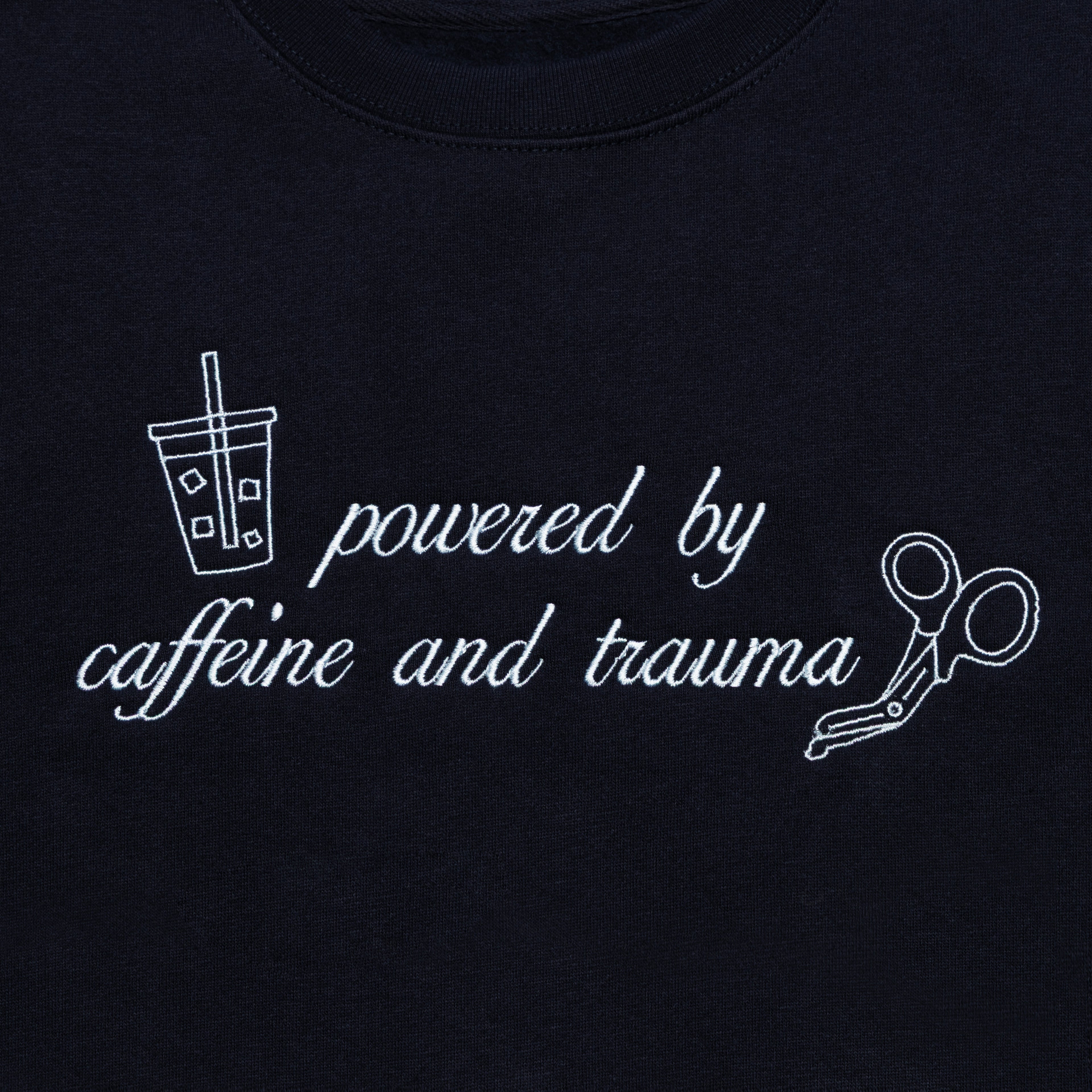 Close-up of the Powered by Caffeine and Trauma design embroidered on the chest of the Classic Navy crewneck